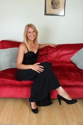 Jentina, blonde mature, pose sur son canapé rouge.